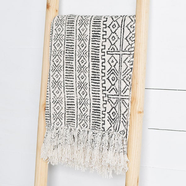 A black and white geometric patterned deco throw with fringes hanging over a wooden frame.