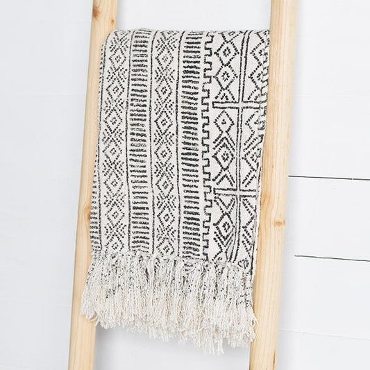 A black and white geometric patterned deco throw with fringes hanging over a wooden frame.