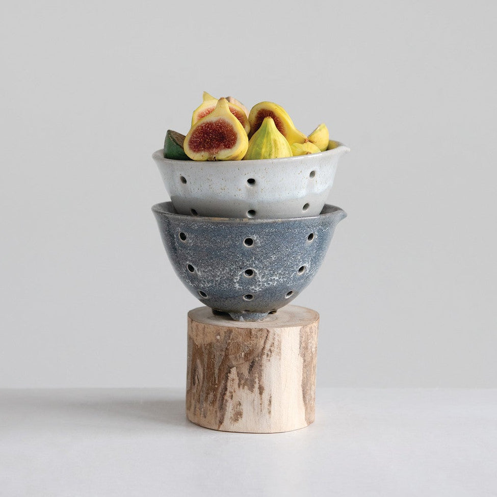 Two stacked ceramic bowls with fruits on a wooden block against a light gray background