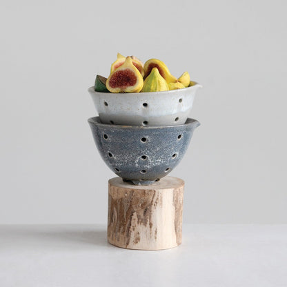 Two stacked ceramic bowls with fruits on a wooden block against a light gray background